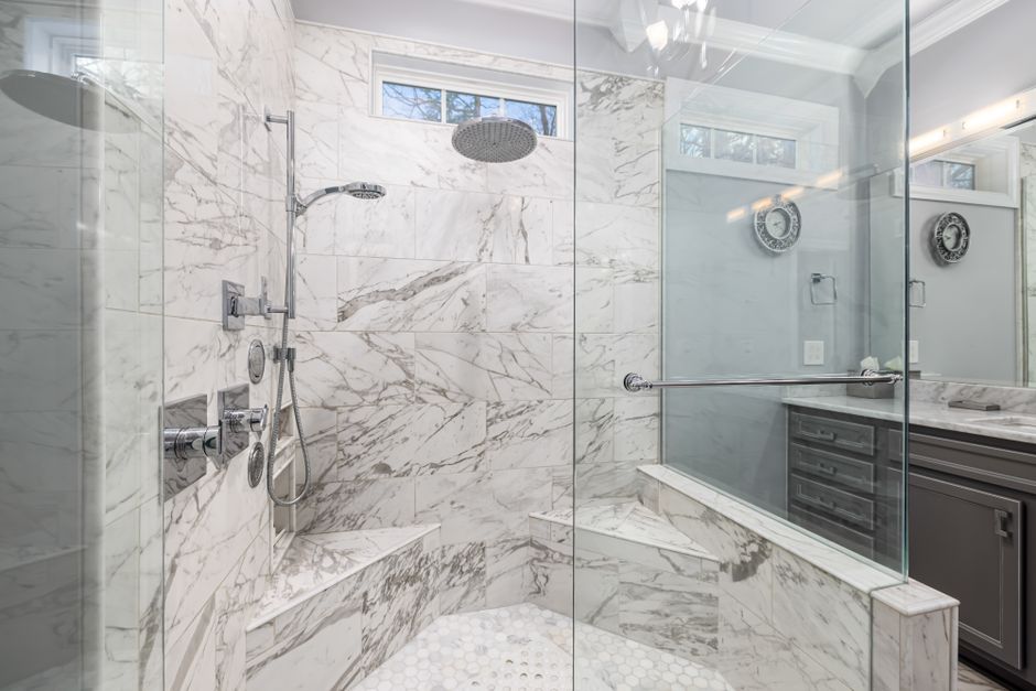 Douche à l'italienne en marbre clair avec banc intégré et barre de maintien